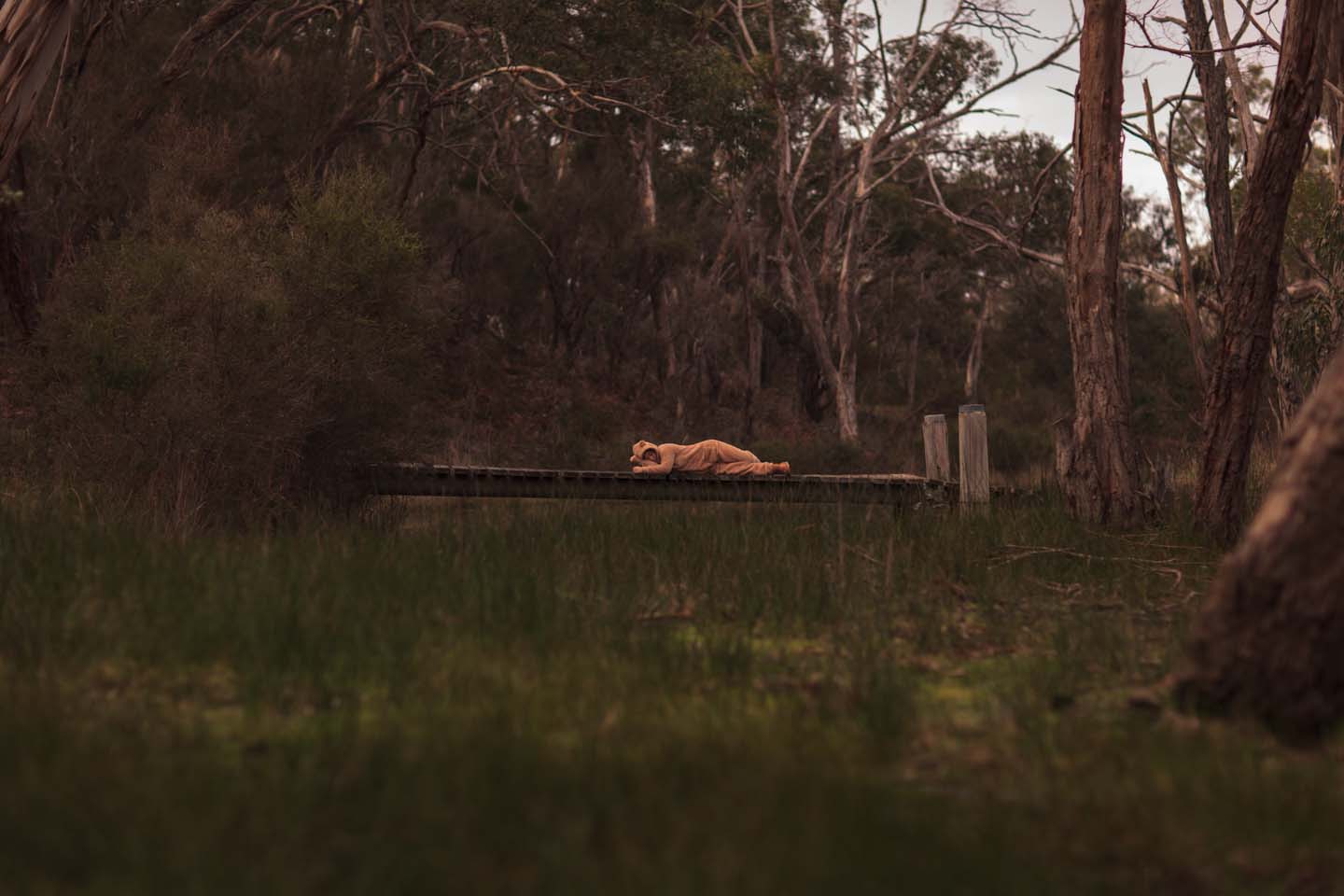 Woman in a onesie suit laying down on a bridge above water Smoke and bush art australia